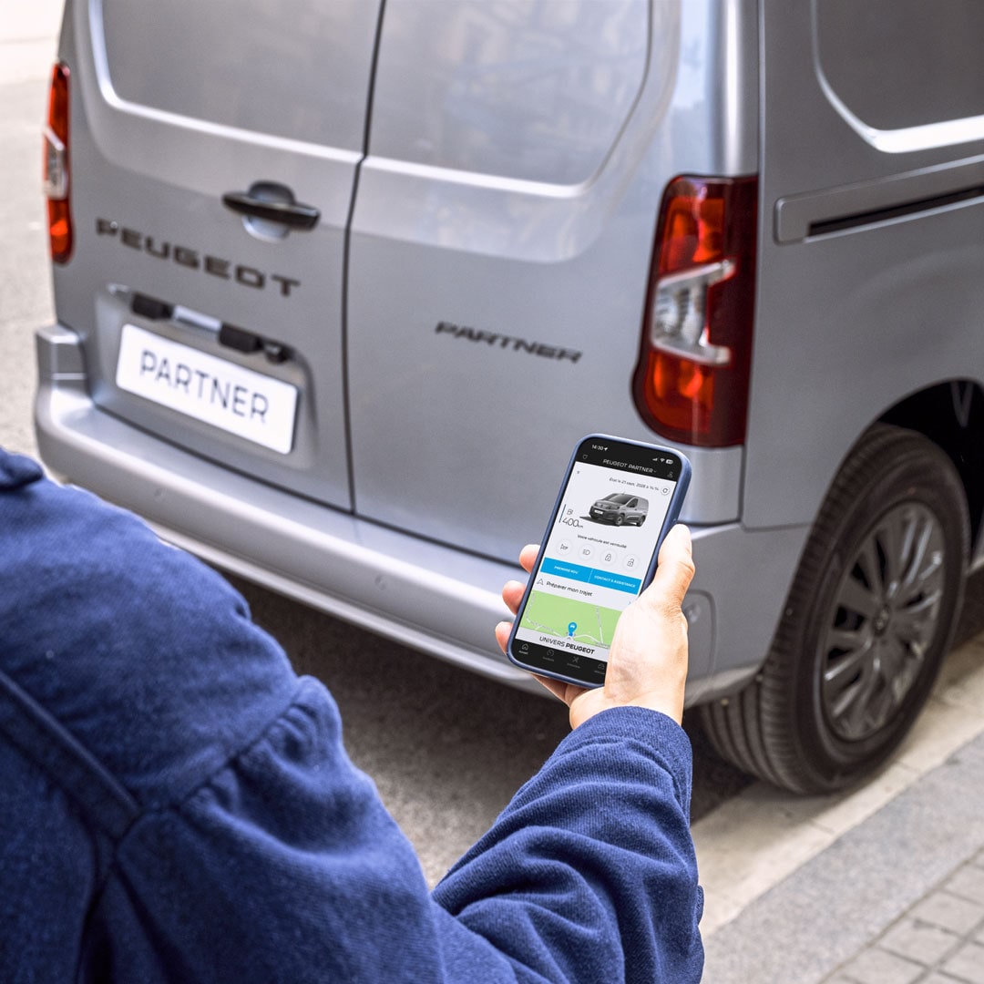 Frau nutzt ein Smartphone hinter dem PEUGEOT Partner